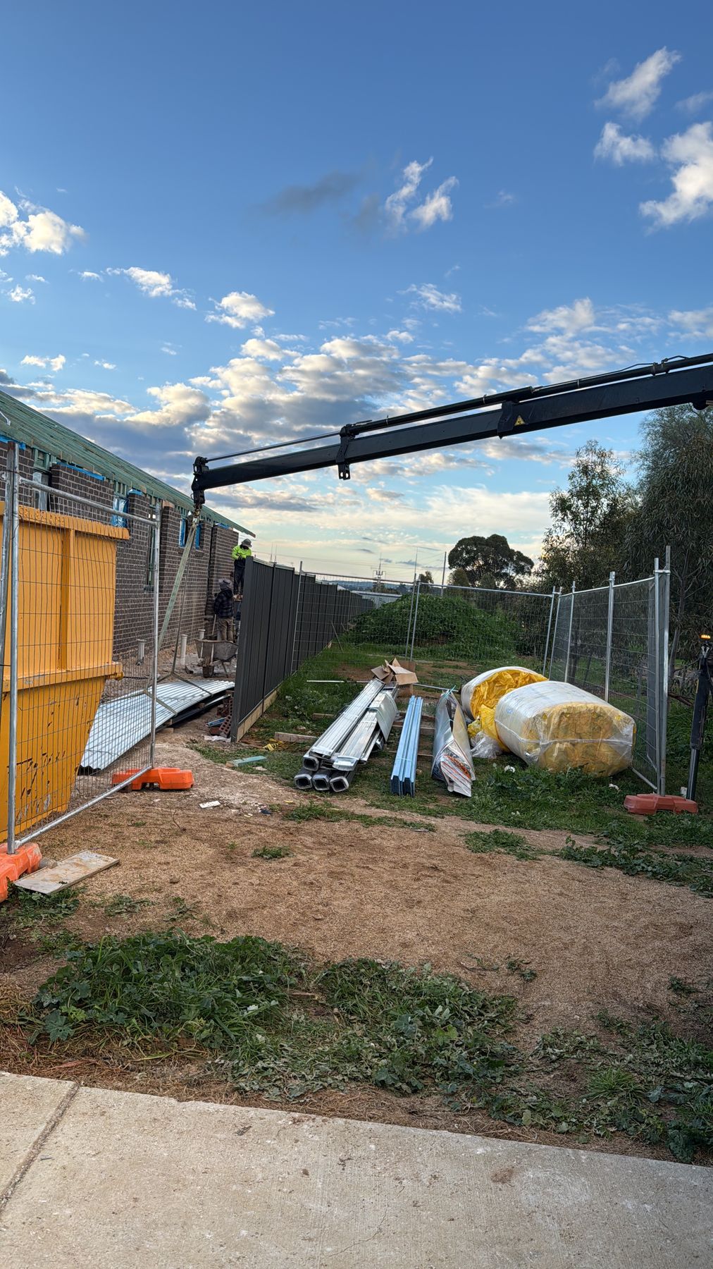 Crane boom reaching over a site fence with materials set down in a backyard