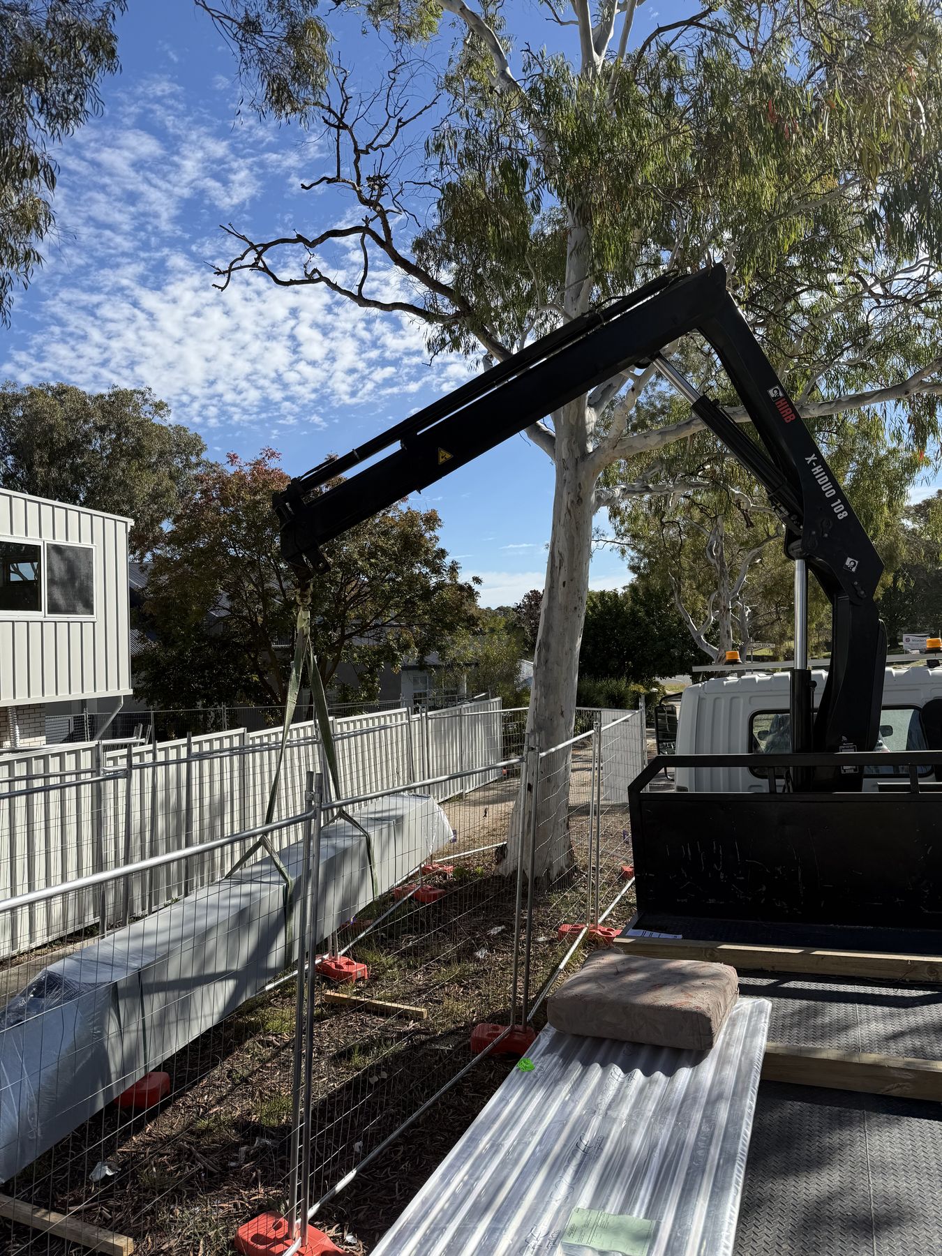 99 Cranes crane truck lifting roofing sheets over a site fence