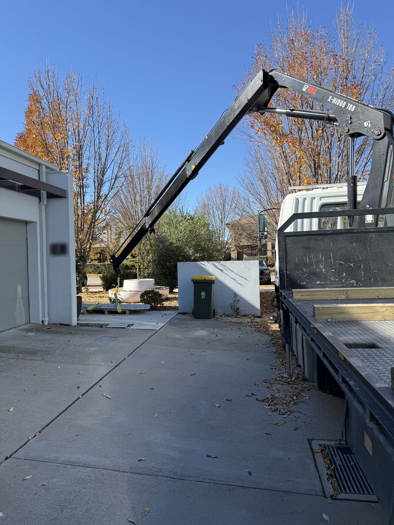 Knuckle-boom crane placing a planter in a residential driveway